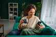 © Miljan Živković - Mature woman relaxing at home using smart phone and drinking coffee