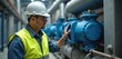 © Maryna - Engineer wearing hard hat and safety vest inspects large industrial cooling system pumps. Man checks pipes and machinery in a factory setting. He controls building climate.