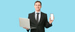 © Pixel-Shot - Happy young businessman with laptop and mobile phone on blue background
