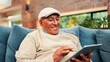 © FlexOn/peopleimages.com - Tablet, happy and senior man on sofa in home with networking, social media or blog post. Relax, digital technology and elderly male person in living room for reading news headline on app in house.
