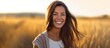 © gufron - Radiant woman smiling in a golden field at sunset.