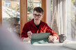 © Westend61 - Man in red shirt using a digital tablet at home during the day