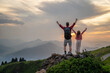 © Westend61 - Father and daughter standing with arms raised on mountain at sunrise
