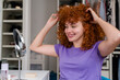 © Westend61 - Woman with curly red hair smiling at her reflection in a mirror at home