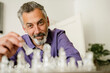 © Westend61 - Man playing chess at home with a thoughtful and smiling expression
