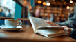 © Masha - Hands, person and reading book in cafe for story, knowledge and student learning literature information in university. Closeup, education and studying novel on coffee shop table at college to relax