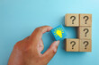 © Pakorn - Creative solution and problem solving concept. Hand chooses a lightbulb block among question marks, symbolizing innovation, smart ideas, strategy, and finding the right answer on a blue background.
