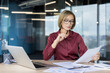 © Liubomir - Businesswoman reviewing financial reports and data on paper, concentrating on her work at a desk with a laptop and various documents in a contemporary office environment