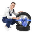 © New Africa - Tire service worker and car wheel with blue ribbon bow on white background. Special offer or discount