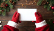 © Rhony - Santa hand holding a blank card mockup on a wooden background with Christmas decorations