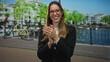 © Krakenimages.com - Woman clapping hands on a street in amsterdam beside a canal and parked bicycles, smiling and wearing red glasses and blazer; celebration happiness.