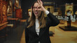 © Krakenimages.com - Woman making ok sign with hand over eye, smiling and wearing red glasses in an art gallery building; playful curiosity.