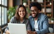 © happy - Two smiling diverse businesspeople using a laptop together at wo. High quality