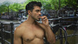 © Krakenimages.com - Man with bare chest and muscular physique smiling while holding snack on street beside canal; healthy enjoyment.