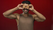 © Krakenimages.com - Young hispanic man wearing a brown tank top smiles while holding cookies over eyes in a red studio; joy.