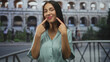 © Krakenimages.com - Woman points fingers to teeth while smiling by colosseum building railing wearing green shirt; travel joy memory.