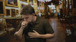 © Krakenimages.com - Young hispanic man clutching throat and coughing into fist while pressing hand to chest in ornate gallery building; health concern distress.