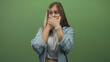 © Krakenimages.com - Blonde woman in denim shirt and white tank top covers mouth with both hands against green studio wall; surprise.