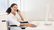 © wavebreak3 - Woman in wheelchair wearing white shirt holding smartphone to ear while using mouse with keyboard
