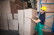 © wavebreak3 - Male warehouse worker in yellow hard hat placing cardboard box onto stack near racking, copy space
