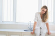 © wavebreak3 - Mid-adult female sitting on countertop near sink, wearing white top, hands resting, copy space