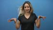 © Krakenimages.com - Young blonde woman shrugging with palms up and slight smirk, wearing black vneck tee in blue studio, frontal pose and visible hands; bemusement questioning.
