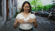 © Krakenimages.com - Woman gesturing with hands on a city street wearing a white ribbed top and blue jeans near parked cars and leafy trees; awkward conversation embarrassment.