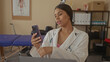 © Krakenimages.com - Woman doctor holds smartphone in clinic with stethoscope draped around neck and blue examination table visible behind her; telehealth empathy.