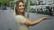 © Krakenimages.com - Smiling woman presenting on city street background, showcasing urban outdoor lifestyle with greenery and people in the distance, creating a lively urban scene.