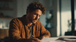 © imagepocket - A focused man with curly hair and a beard diligently reviews documents, writing at his desk in warm, subdued lighting, tackling paperwork.