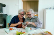© Davor - Senior couple using smartphone at home kitchen, focused and curious
