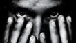 © Nad - A man covers his face with his hands, revealing only his intense eyes. The black and white style emphasizes the emotion and tension in the scene, creating a striking visual effect.