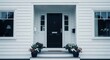 © mlangsen - Front view of a neat white clapboard house with a black door, steps, and potted flowers