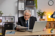 © Andrii Iemelianenko - Senior freelancer accountant working with financial graph documents, calculate taxes for charts and reports at home office desk. Businessman grandpa working on laptop computer planning expenses budget