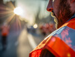 © Mr. Orsetto - Male construction worker wearing bright safety vest with sunlight glowing in the background on a busy urban street during golden hour