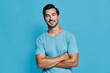 © SHOTPRIME STUDIO - Smiling cheerful young man with crossed arms wearing a light blue shirt, looking at the camera against a bright blue background, exuding a friendly vibe.