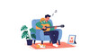 © Farhan - A relaxed young man sits in a comfortable armchair at home, playing an acoustic guitar with two cute cats resting peacefully beside him.