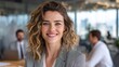 © Johannes - friendly businesswoman in a modern office space smiling confidently with coworkers working in the background on a bright day showcasing teamwork and professionalism