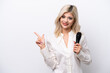 © luismolinero - Young singer woman picking up a microphone isolated on white background pointing to the side to present a product