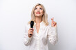 © luismolinero - Young singer woman picking up a microphone isolated on white background with fingers crossing and wishing the best