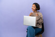© luismolinero - Young mixed race woman sitting on a chair with laptop isolated on purple background surprised and pointing front