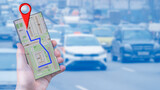 A man's hand holds a smartphone with an online map, on which a destination is marked. In the background, a busy road is shown. The concept of internet navigation and modern technology is represented