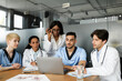© Prostock-studio - Professional multiracial team of doctors concentrated men and women in workwerar sitting at table, looking at notebook screen, taking notes, looking for solutions, clinic interior