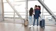 © Prostock-studio - A family stands together in an airport terminal. The children are excited, pointing at an airplane as it takes off. Their luggage is beside them as they wait to travel.