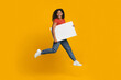 © Prostock-studio - A joyful woman in a red shirt and blue jeans is running while holding a blank sign. The bright yellow background adds to the cheerful atmosphere of the scene.