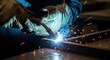 © Tortuga - Industrial worker welding metal structure with bright sparks in a dark factory workshop