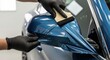 © Tortuga - Car wrapping specialist putting blue vinyl foil on car mirror in workshop using a squeegee tool