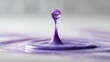 © Tina - A close-up of a purple water droplet creating a splash in a shallow pool of purple liquid. The background is blurred, emphasizing the droplet's shape and color.