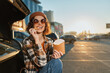© SHOTPRIME STUDIO - woman eats fries by car trunk in parking lot, smile and sunglasses catching sunlight as she sits in beanie and plaid jacket at golden hour authenticity, candid lifestyle, golden hour glow, mindful