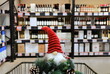 © rospoint - Funny Christmas gnome and wreath on a supermarket trolley. Shopping cart, shelves with bottles of alcohol, food, groceries. Shopping in shop, New Year sale, elite alcohol department for party